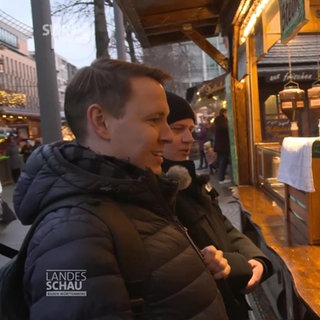 Zwei Lebensmittelkontrolleure stehen am Bratwurststand auf dem Mannheimer Weihnachtsmarkt