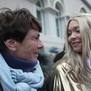 Sonja Faber-Schrecklein lächelt eine junge Frau an, die als Christkind verkleidet ist und eine Krone und einen goldenen Umhang trägt.