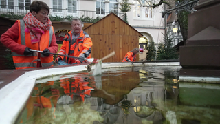 Sonja Faber-Schrecklein steht an einem Brunnen in Bad Wimpfen und fischt mit einer Greifzange Müll aus dem Wasser.