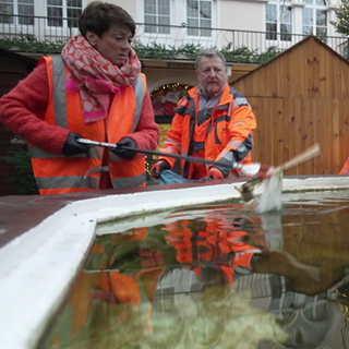 Sonja Faber-Schrecklein steht an einem Brunnen in Bad Wimpfen und fischt mit einer Greifzange Müll aus dem Wasser.