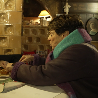 Sonja Faber-Schrecklein sitzt mit einem Mann an einem Tisch. Sie greifen beide zu einem Teller. Im Hintergrund ist ein heller Kachelofen.