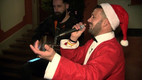 Postbote Vincenzo Spagnuolo trägt ein Weihnachtsmannkostüm und singt in ein Mikrofon.