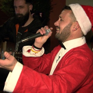 Postbote Vincenzo Spagnuolo trägt ein Weihnachtsmannkostüm und singt in ein Mikrofon.