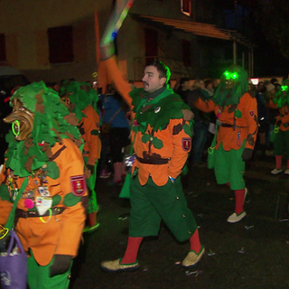 Verkleidete Menschen ziehen in einem bunten Fasnachtsumzug durch das Dorf, umringt von jubelnden Zuschauern.