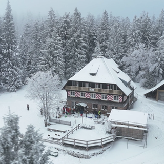 Gäste in einer Skibar genießen Après-Ski-Stimmung, lachen und stoßen miteinander an, während im Hintergrund die gemütliche Hüttengaststube zu sehen ist.