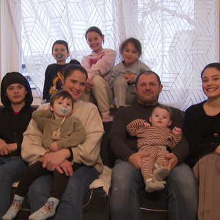 Die neunköpfige Familie Bajgora sitzt gemeinsam auf dem Sofa und lächelt in die Kamera.