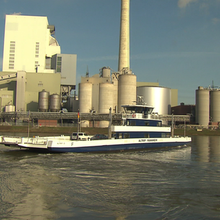 Die neue Rheinfähre „Alma“ fährt auf dem Rhein, im Hintergrund sind Industrieanlagen zu sehen.