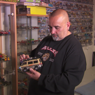 Franco Baldassarre steht vor seiner riesigen Modellauto-Sammlung und hält ein Auto in der Hand, umgeben von unzähligen bunten Miniaturen.