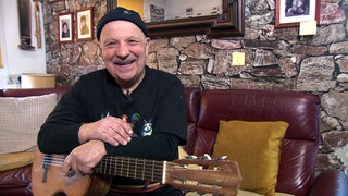 Der 76-jährige Yusuf Cavak hält seine Gitarre und lächtelt in die Kamera.