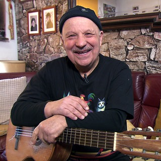 Der 76-jährige Yusuf Cavak hält seine Gitarre und lächtelt in die Kamera.