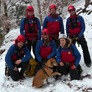 Bergwacht rettet Hund Leo - fünf Männer und eine Frau in Bergwachtausrüstung machen ein Gruppenfoto mit dem Hund. Es liegt Schnee.
