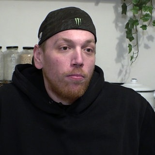 Daniel trägt eine Baseballcap und einen schwarzen Pullover. Er sitzt in der Küche.