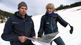 Skiliftbetreiber Matthias Schneider und Andrea Brender stehen im Schnee auf der Skipiste. Sie halten einen Landschaftsplan in der Hand.