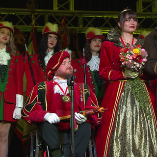 Eine Fasnet-Gesellschaft. Die Fasnetsprinzessin steht neben dem Fasnetsprinzen. Er sitzt im Rollstuhl.