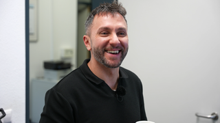 Ein Mann, Hora Soruika, lacht in die Kamera. Er trägt ein schwarzes Shirt.