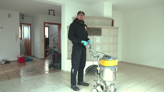 Andreas Röhrich steht in Arbeitskleidung in einem leeren Raum mit einem großen Gerät. Damit kann man schwere Verschmutzungen entfernen. 