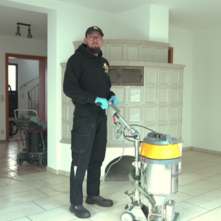 Andreas Röhrich steht in Arbeitskleidung in einem leeren Raum mit einem großen Gerät. Damit kann man schwere Verschmutzungen entfernen. 