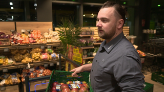 Mitarbeiter im Supermarkt räumt Äpfel ins Regal