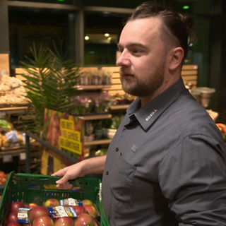 Mitarbeiter im Supermarkt räumt Äpfel ins Regal