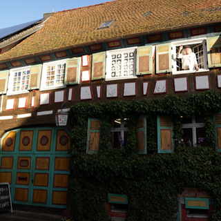 Mann winkt aus dem Fenster eines bunten Fachwerhauses