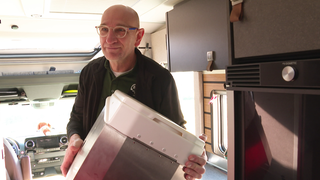 Sascha Gerner hat seine selbsterfundene Campingtoilette in der Hand. Er steigt in einen Campingwagen. 