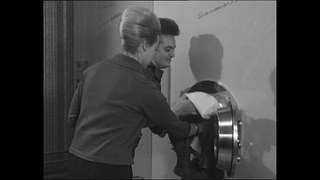 Waschsalon in den 60er Jahren. Ein Paar befüllt die Waschmaschine.