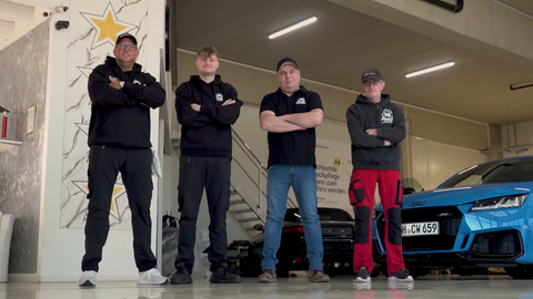 Autopfleger Daniel Kampmann, Sohn Niklas, mit Matze und Uwe stehen nebeneinander in der Werkstatt. Hinter ihnen stehen Autos.