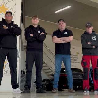 Autopfleger Daniel Kampmann, Sohn Niklas, mit Matze und Uwe stehen nebeneinander in der Werkstatt. Hinter ihnen stehen Autos.
