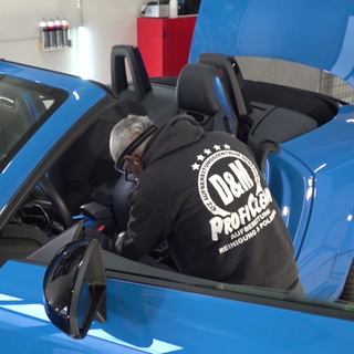 Ein Mitarbeiter von Daniel Kampmann reinigt ein blaues Auto in der Werkstatt.