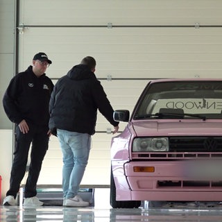 Daniel Kampmann mit Kunden stehen neben einem pinken VW.