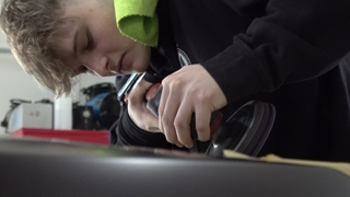 Niklas poliert den Spoiler eines schwarzen Autos. Über seiner Schulter hängt ein grünes Handtuch.