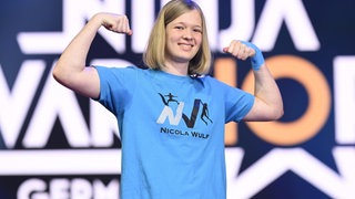 Nicola Wulf mit angespanntem Bizeps in einem blauen T-Shirt.