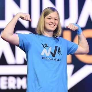 Nicola Wulf mit angespanntem Bizeps in einem blauen T-Shirt.