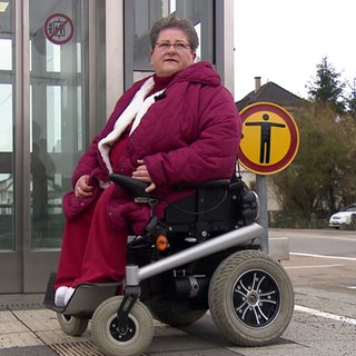 Frau im Rollstuhl steht vor Aufzug am Bahnhof.