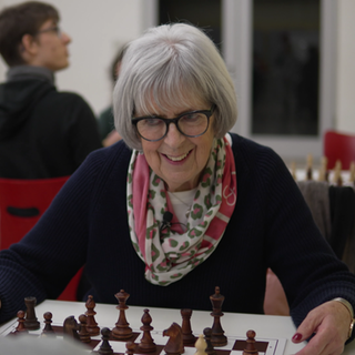 Schach-Oma sitzt am Tisch und spielt Schach mit einem Kind.