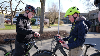 Zwei 12-Jährigen (Amos und Niklas) stehen sich mit ihren Fahrrädern gegenüber. Beide tragen einen Fahrradhelm und halten ihren Blick auf die Lenker.