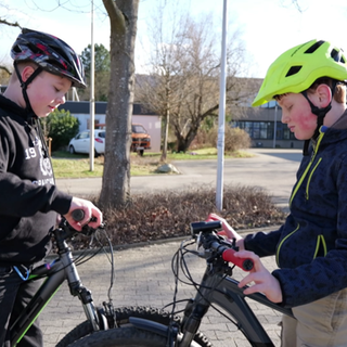 Zwei 12-Jährigen (Amos und Niklas) stehen sich mit ihren Fahrrädern gegenüber. Beide tragen einen Fahrradhelm und halten ihren Blick auf die Lenker.
