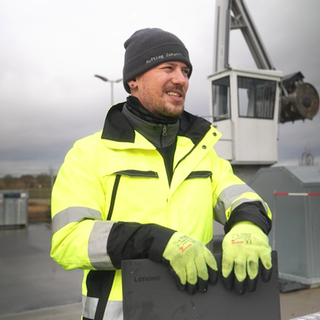 Arno Heinzmann steht auf einem Wertstoffhof. Er trägt eine neongelbe Warnweste. 
