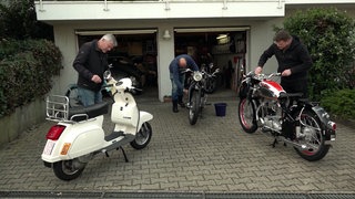 Drei Motorrad-Fans arbeiten an in einer Einfahrt an ihren Mottorädern, Mopeds und Rollern.