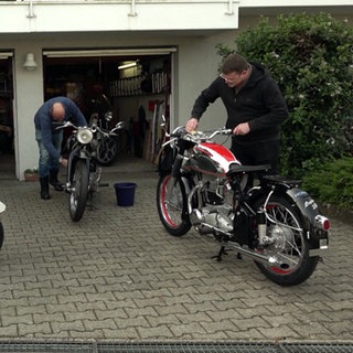 Drei Motorrad-Fans arbeiten an in einer Einfahrt an ihren Mottorädern, Mopeds und Rollern.