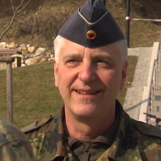 General Thomas Seifert trägt seine Bundeswehr-Uniform und lächelt einen Soldaten an, der mit dem Rücken zur Kamera steht.