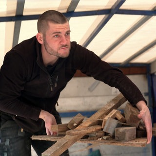 Simon steht in einem Anhänger und trägt einen Haufen Bauschutt in beiden Händen.