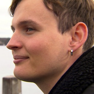 Marian Grau schaut zur linken Bildseite. Im Hintergrund sieht man verschwommen den Bodensee.