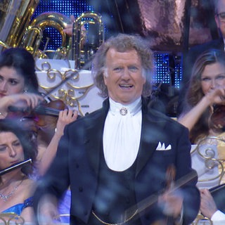 André Rieu steht in der Stuttgarter Schleyer-Halle. Im Hintergrund ist ein Orchester zu sehen. 