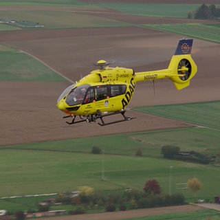 Der gelbe ADAC-Rettungsheli Christoph 22 fliegt über ein Feld.