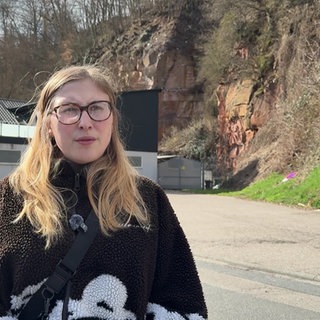 Adriana Dobihal steht vor ihrem Haus, was im Hintergrund leicht unscharf ist. Rechts des Hauses steht eine gelbe Sandsteinwand.