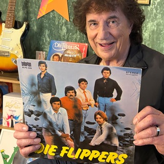 Olaf der Flipper hält eine Schallplattenhülle mit der Aufschrift "Die Flippers" in die Kamera.