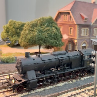 Eine Modell-Lokomotive der Brenztalbahn steht auf den Gleisen. Im Hintergrund ist eine Miniatur-Nachbildung eines Backsteinhauses zu sehen, dass den Sontheimer Bahnhof darstellen soll.