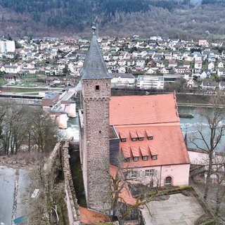 Eine Backstein-Kirch ein Eberbach steht auf einem Hügel. Im Hintergrund ist eine Stadt zu sehen, die Burg 