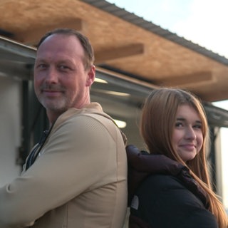 Kai und Madita stehen Rücken an Rücken vor ihrem Foodtruck und schauen in die Kamera.